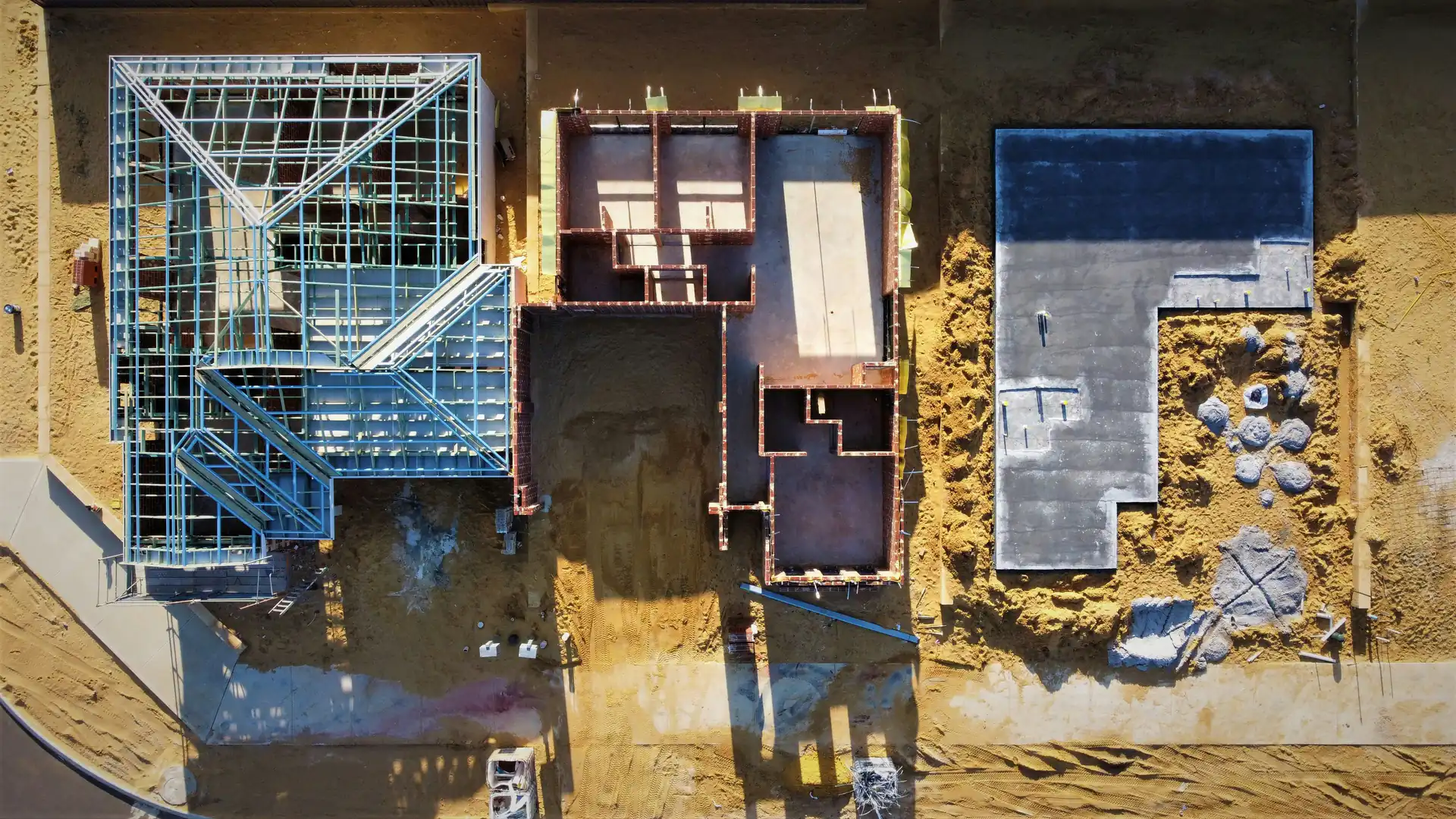 Aerial view of three house plots at slab, brick and roof-frame stage